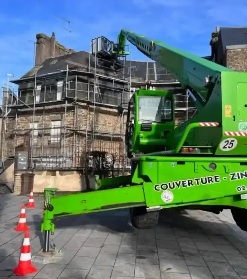 Engin de levage vert devant un bâtiment ancien en pierre sous échafaudage