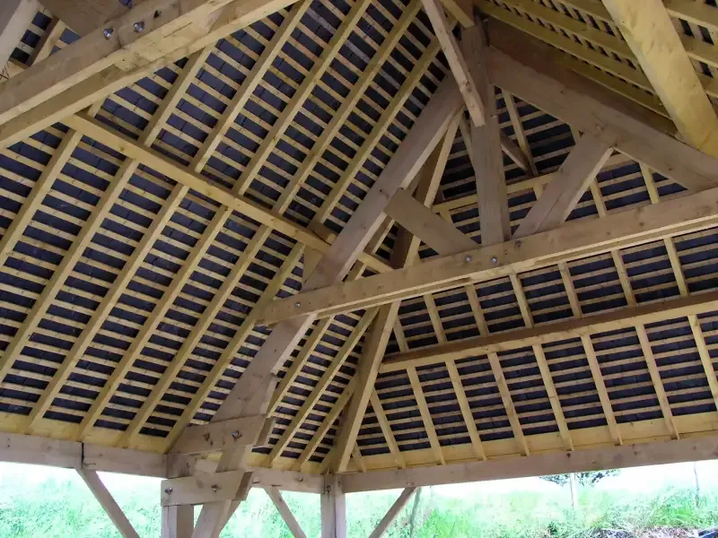 Structure de charpente en bois visible sous une toiture en construction.