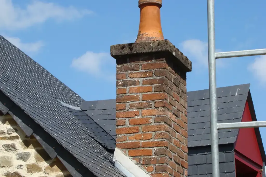 Cheminée en briques sur une toiture en ardoise, avec un échafaudage visible sous un ciel dégagé