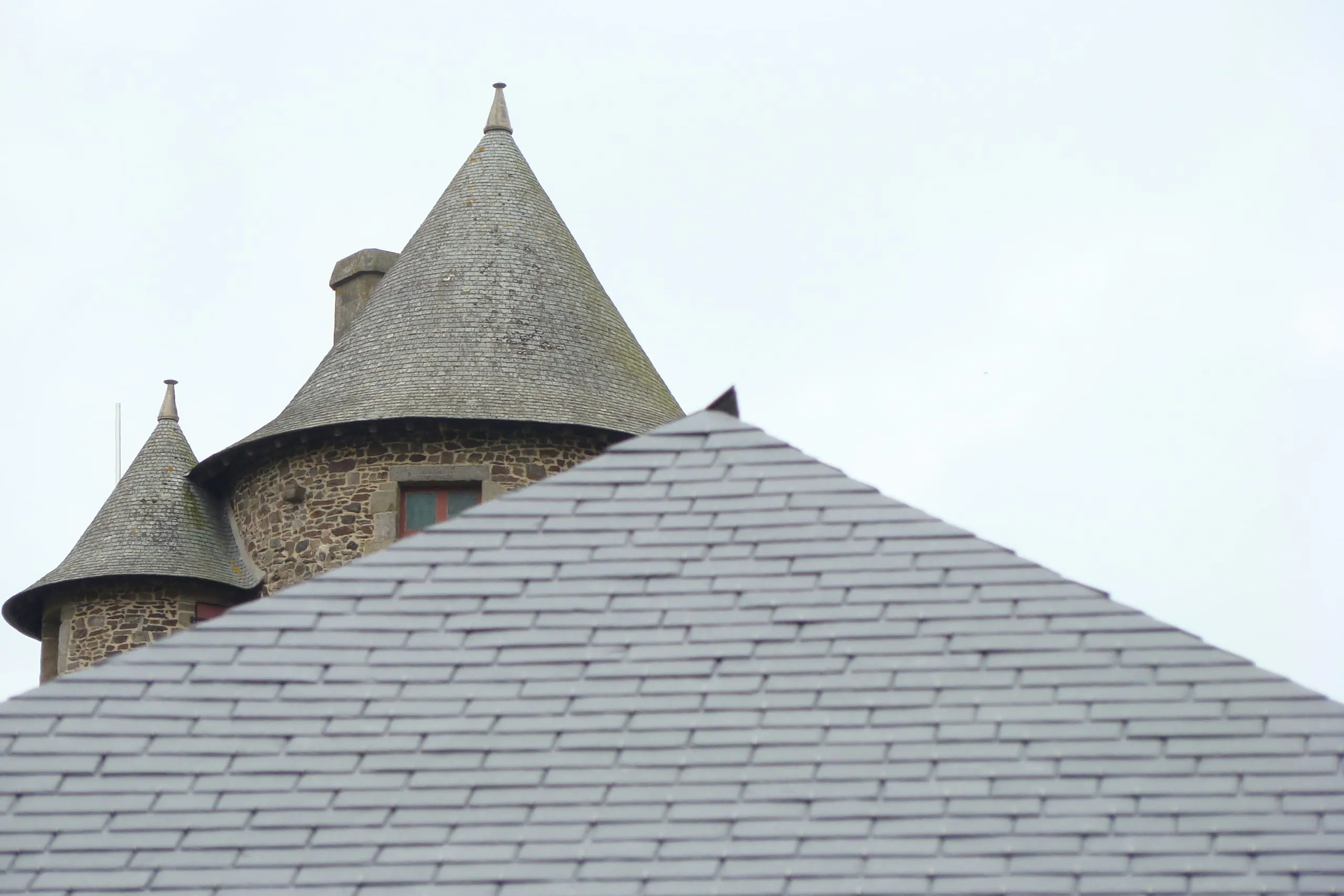 Tourelles en pierre coiffées d'ardoise derrière un pan de toiture neuf