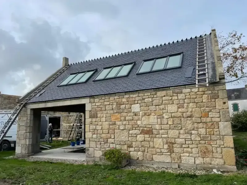 Toiture en ardoise équipée de plusieurs fenêtres de toit Velux sur une maison en pierre, sous un ciel nuageux.
