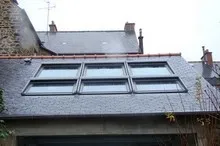 Toiture en ardoise équipée de plusieurs fenêtres de toit panoramiques, entre des façades en pierre