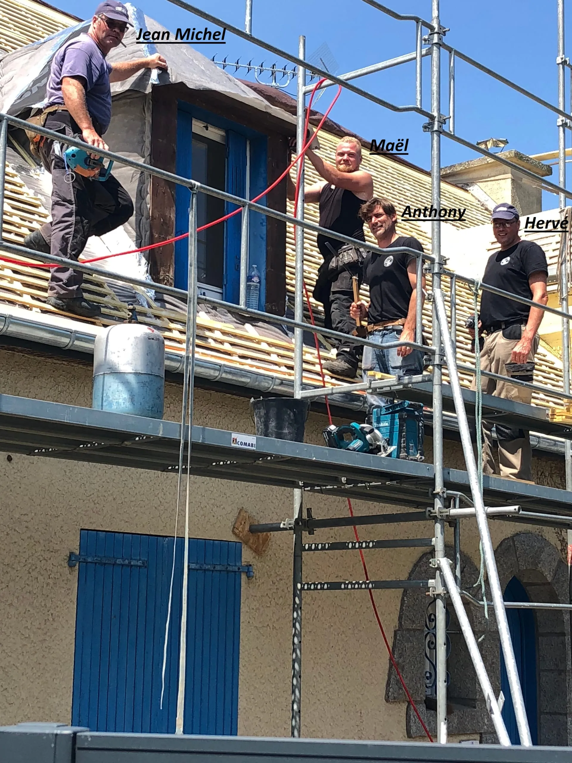 Quatre couvreurs sur un échafaudage devant une lucarne dont le toit est en cours de pose sur lattis