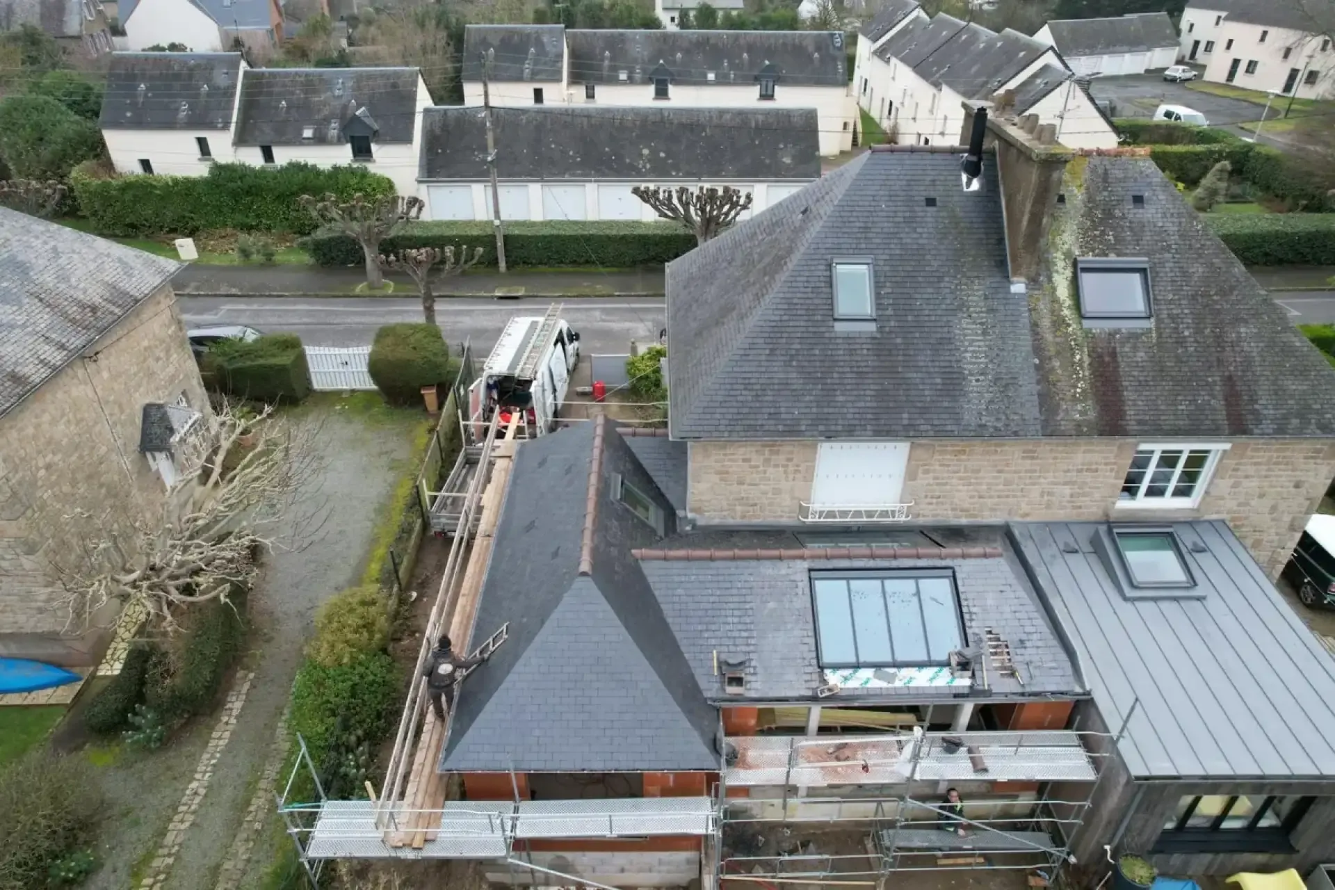 Vue aérienne d'une extension en ardoise avec deux verrières, accolée à une maison en pierre, avec échafaudage