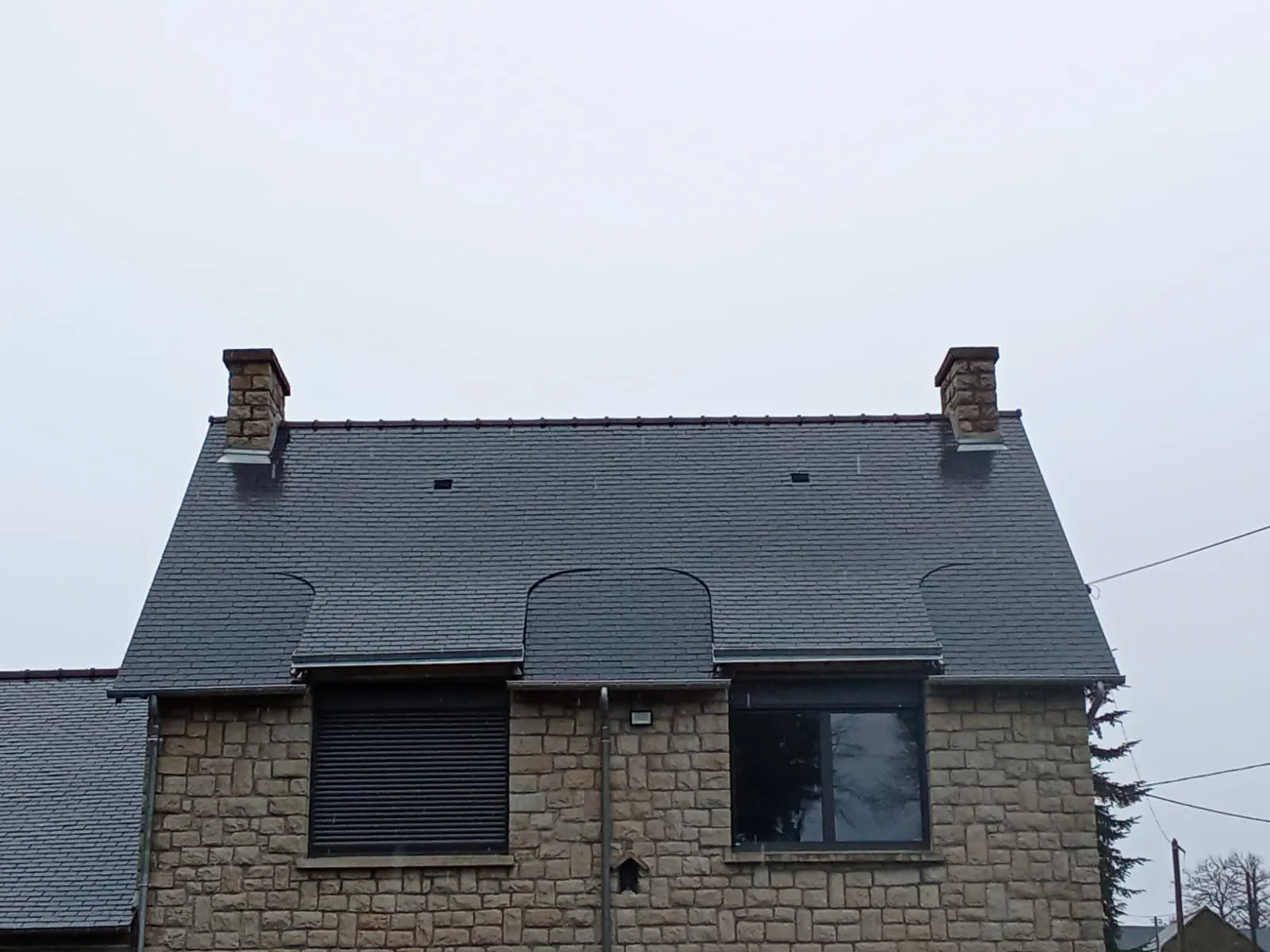 Maison en pierre avec toiture en ardoise, deux cheminées et lucarne