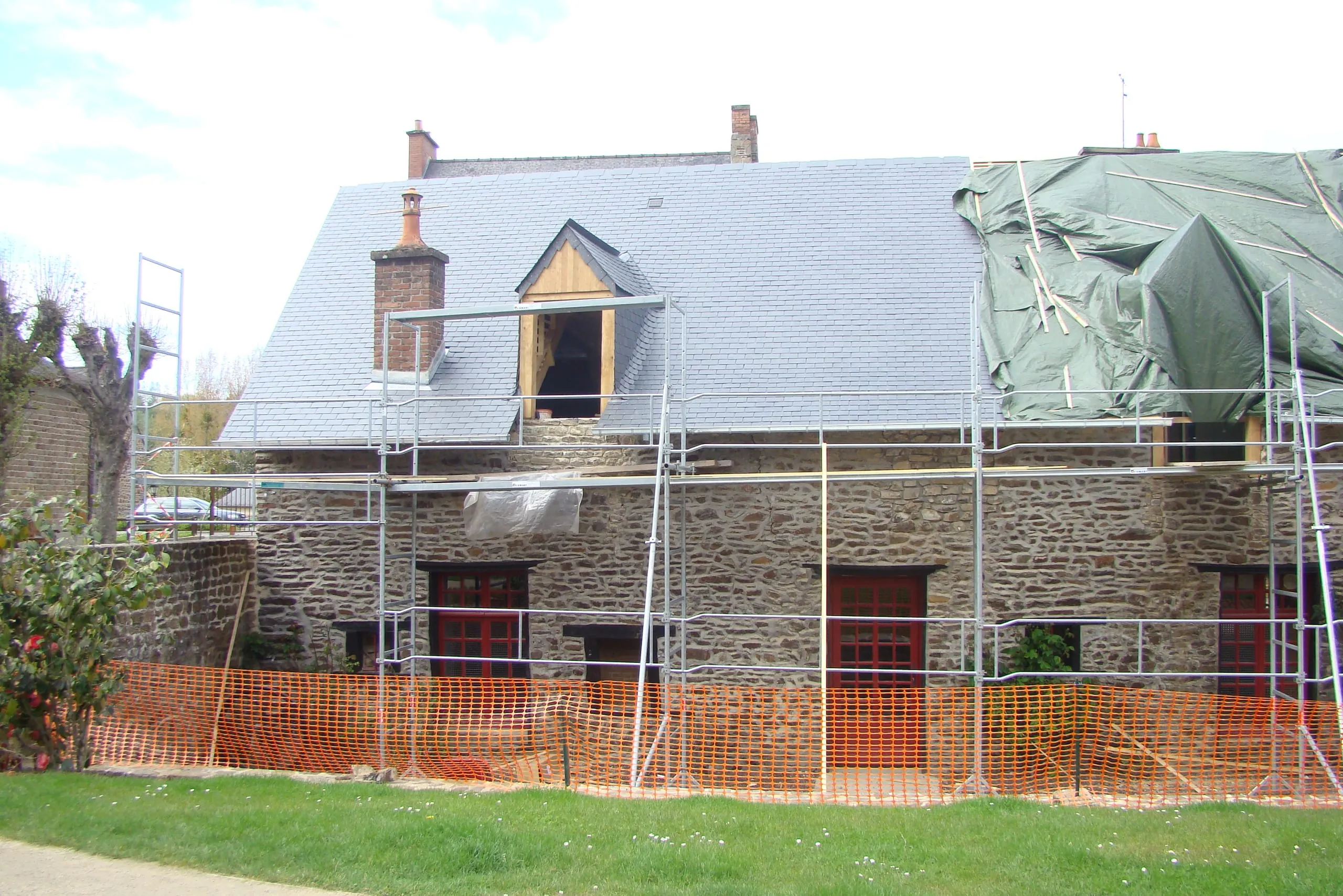 Maison en pierre sous échafaudage, toiture en ardoise posée à gauche et partie droite encore bâchée