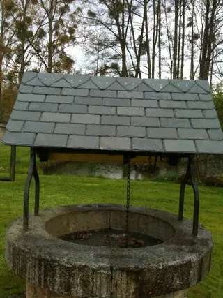 Margelle de puits en pierre coiffée d'un petit toit en ardoise