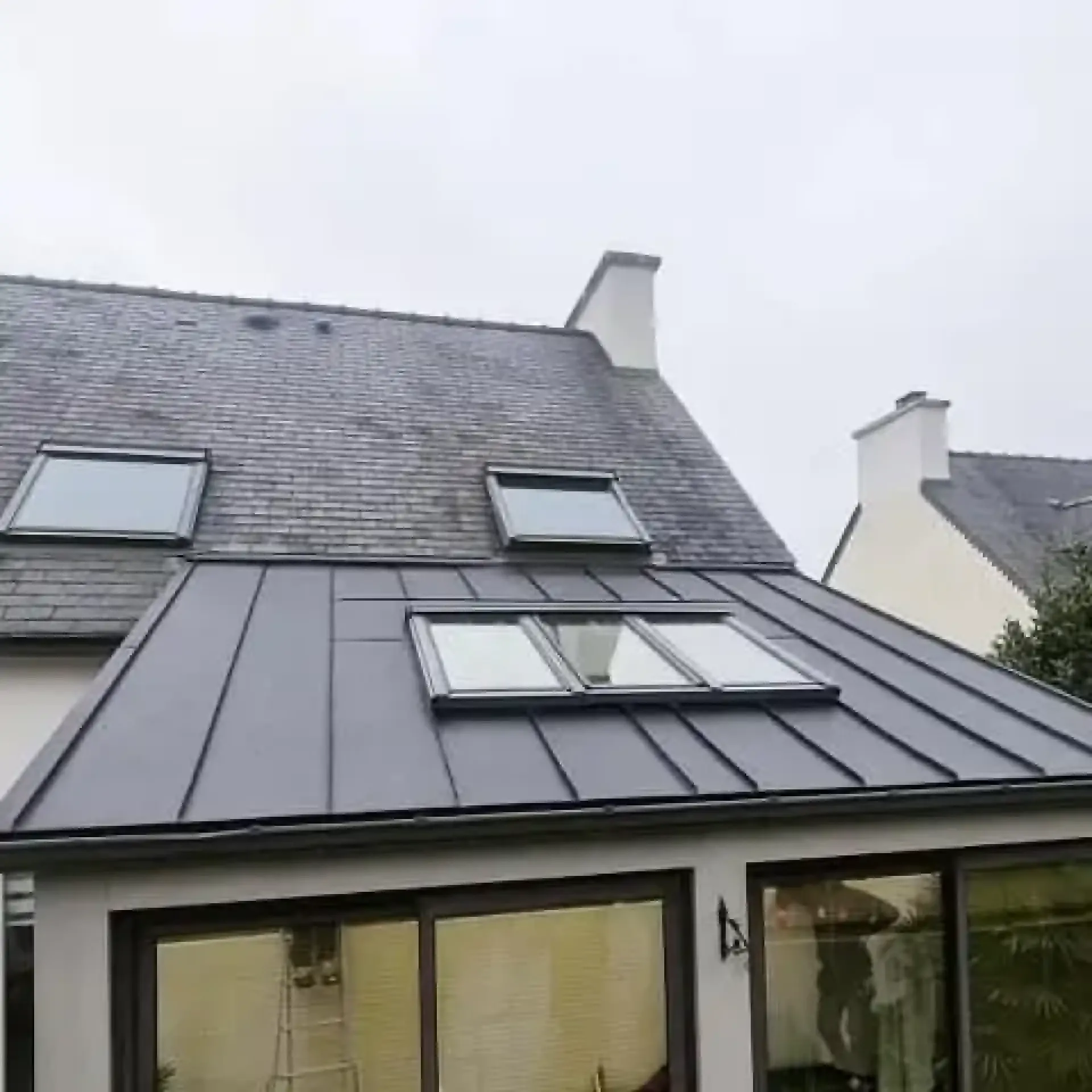 Toiture en ardoise et zinc anthracite équipée de plusieurs châssis de toit au-dessus d'une véranda